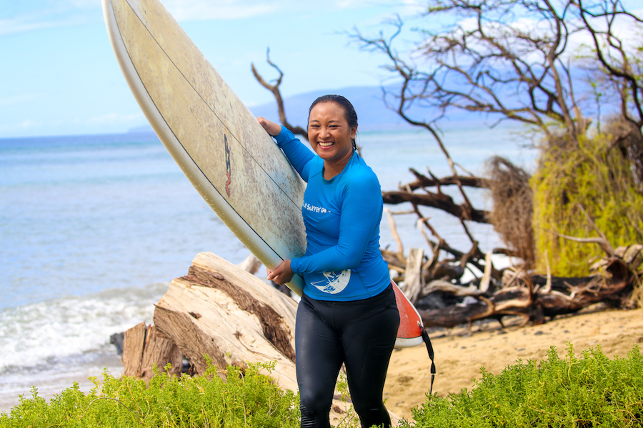 mask mandate ends in Hawaii - a female surfer carrying a board smiles. 